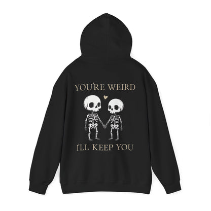 Two skeletons holding hands with a red heart, quirky “You’re Weird I’ll Keep You” text, gothic skeleton couple hoodie by SkeletonWear Apparel