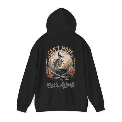 Relaxed skeleton cradling black cat with eyes closed – cozy gothic fall hoodie by SkeletonWear Apparel