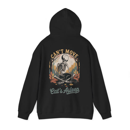 Relaxed skeleton cradling black cat with eyes closed – cozy gothic fall hoodie by SkeletonWear Apparel