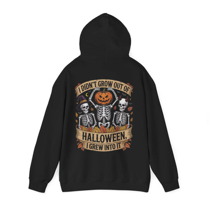 Skeletons with pumpkin, witch hat, and devil horns under banner ‘I Didn’t Grow Out of Halloween, I Grew Into It’ – SkeletonWear Apparel Halloween hoodie design
